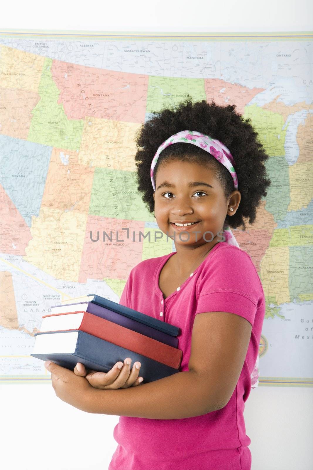 African American girl standing in front of USA map holding stack of books smiling at viewer.