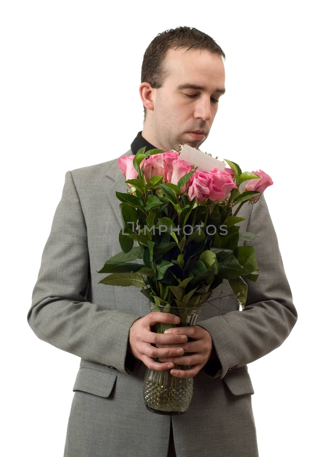 A young man wearing a formal suit is smelling some roses in a vase, isolated against a white background