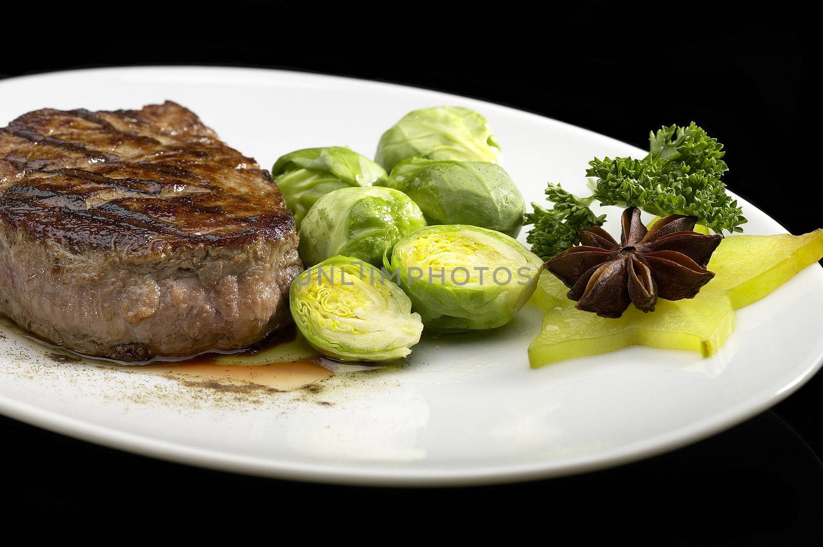 juicy filet mignon on plate with brussel sprout over black background