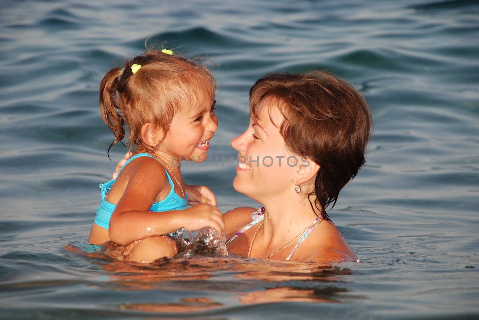 On the sea. Joyful mum hold in hands the laughing daughter over water 