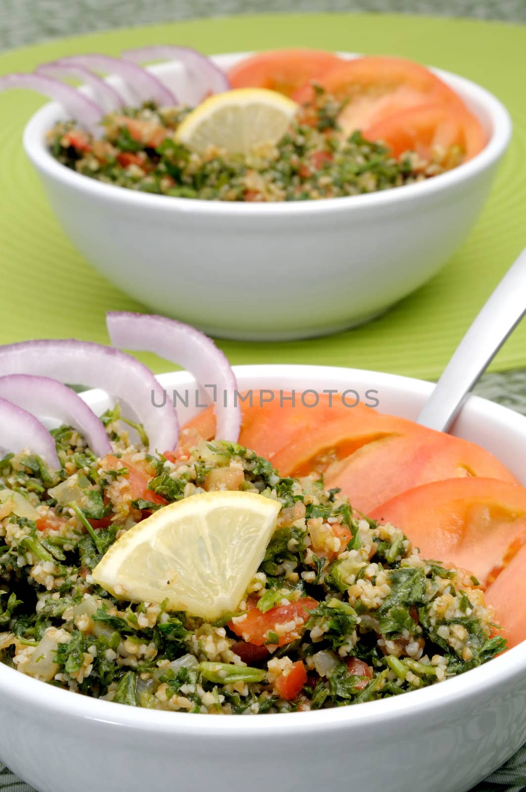Tabbouleh with tomato and onion slices and lemon in white bowls