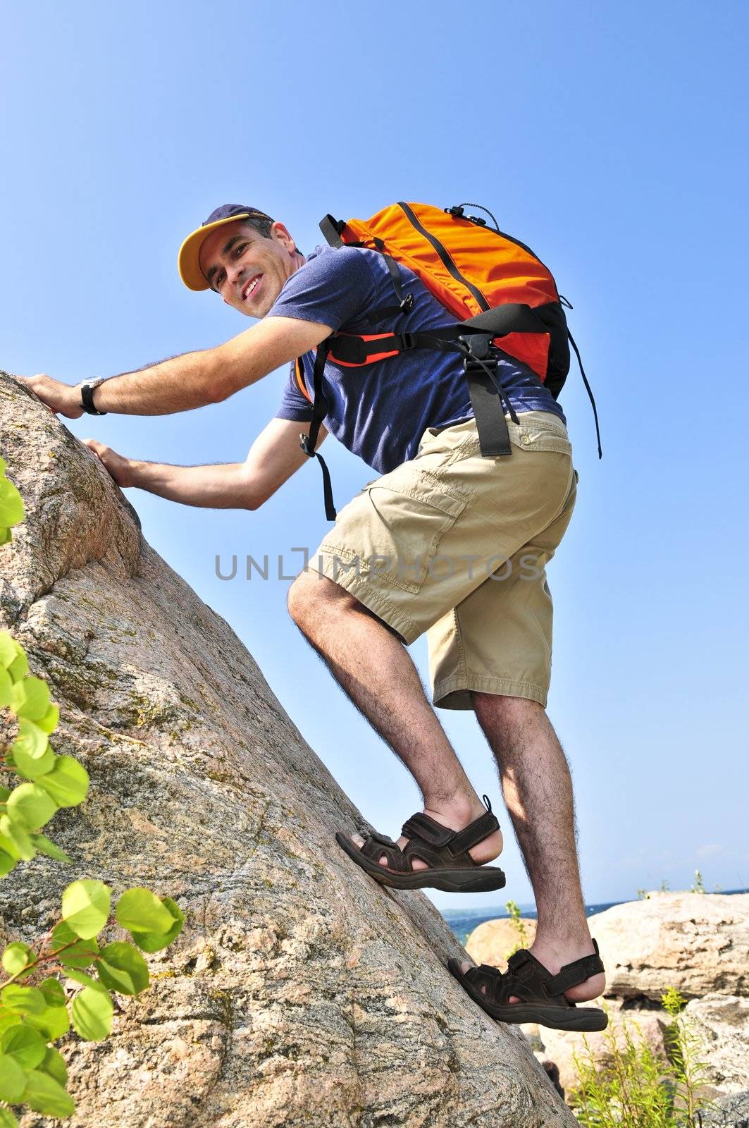 Middle aged man with backpack climbing a rock