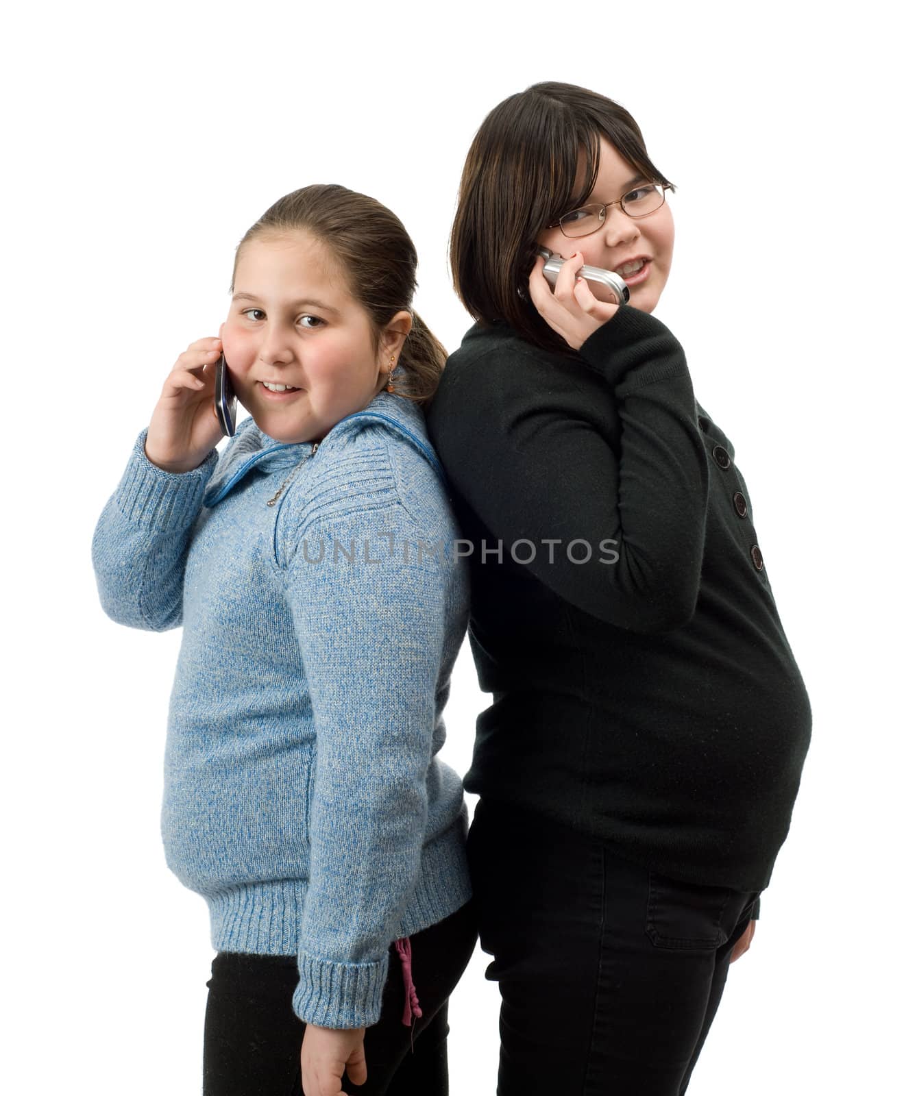 Two young girls standing back to back, talking on their cell phones, isolated against a white background