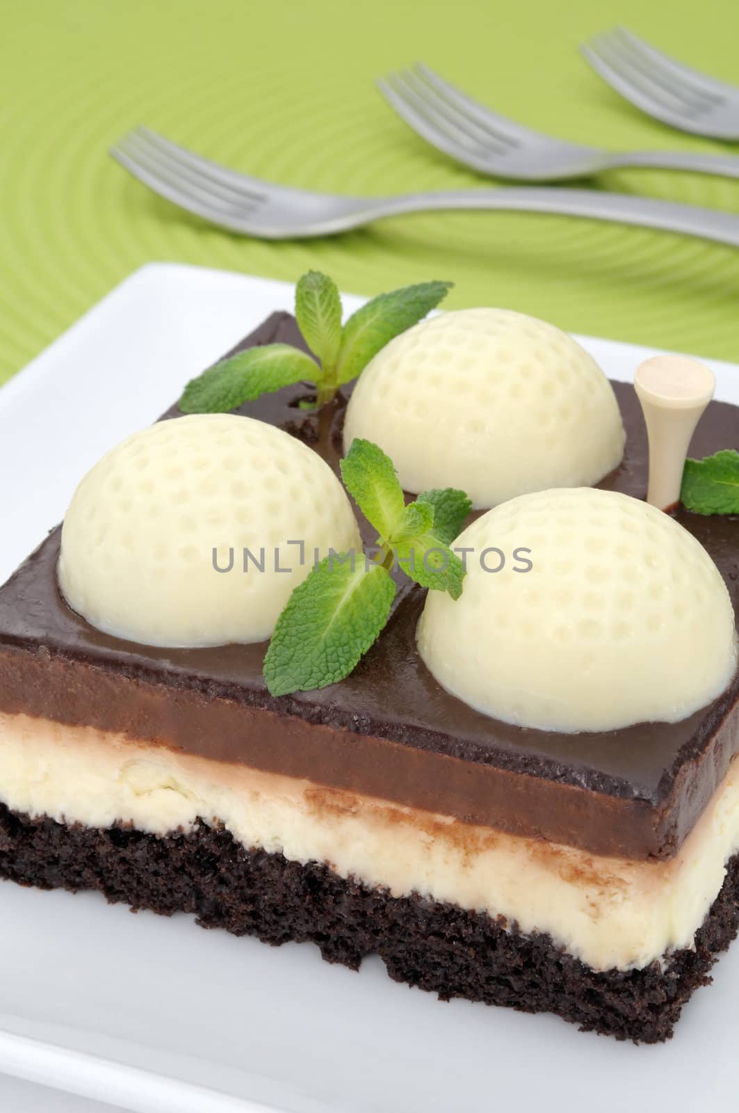 Fanciful chocolate golf cake with mint leaves on a green mat with forks