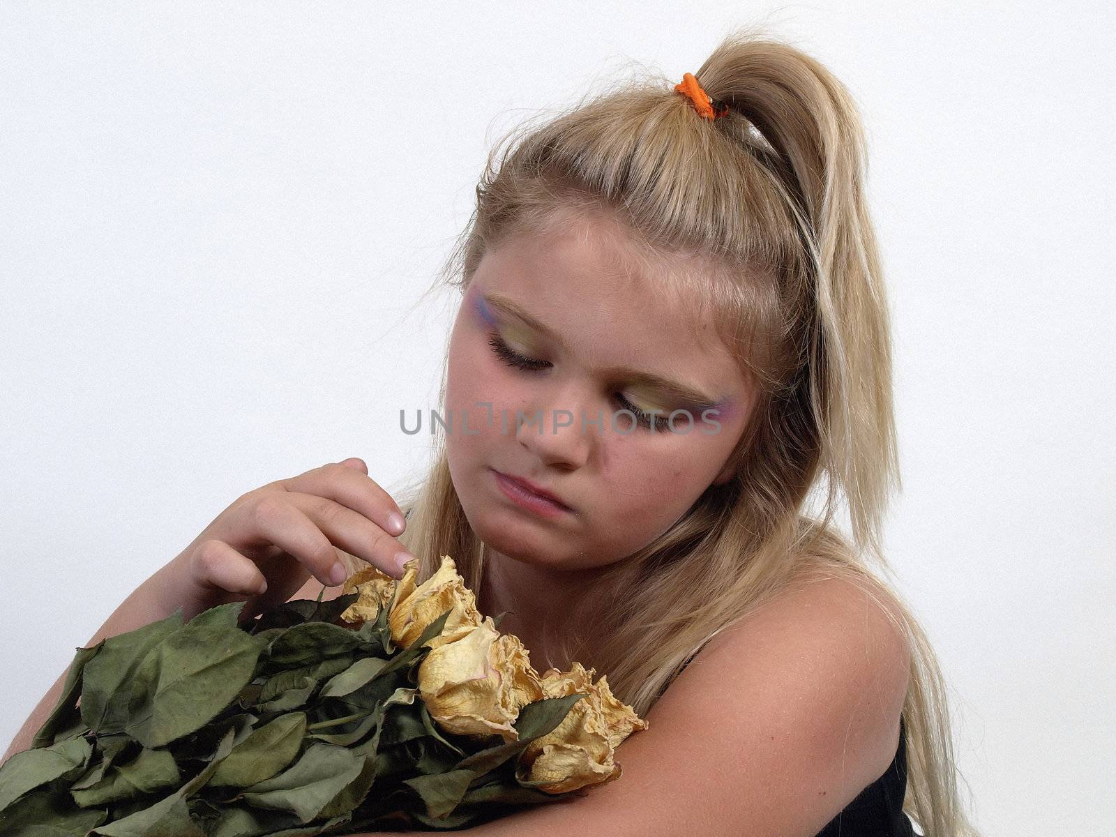 A young blonde girl thoughtfully touches a bouquet of dried roses in her arms.
