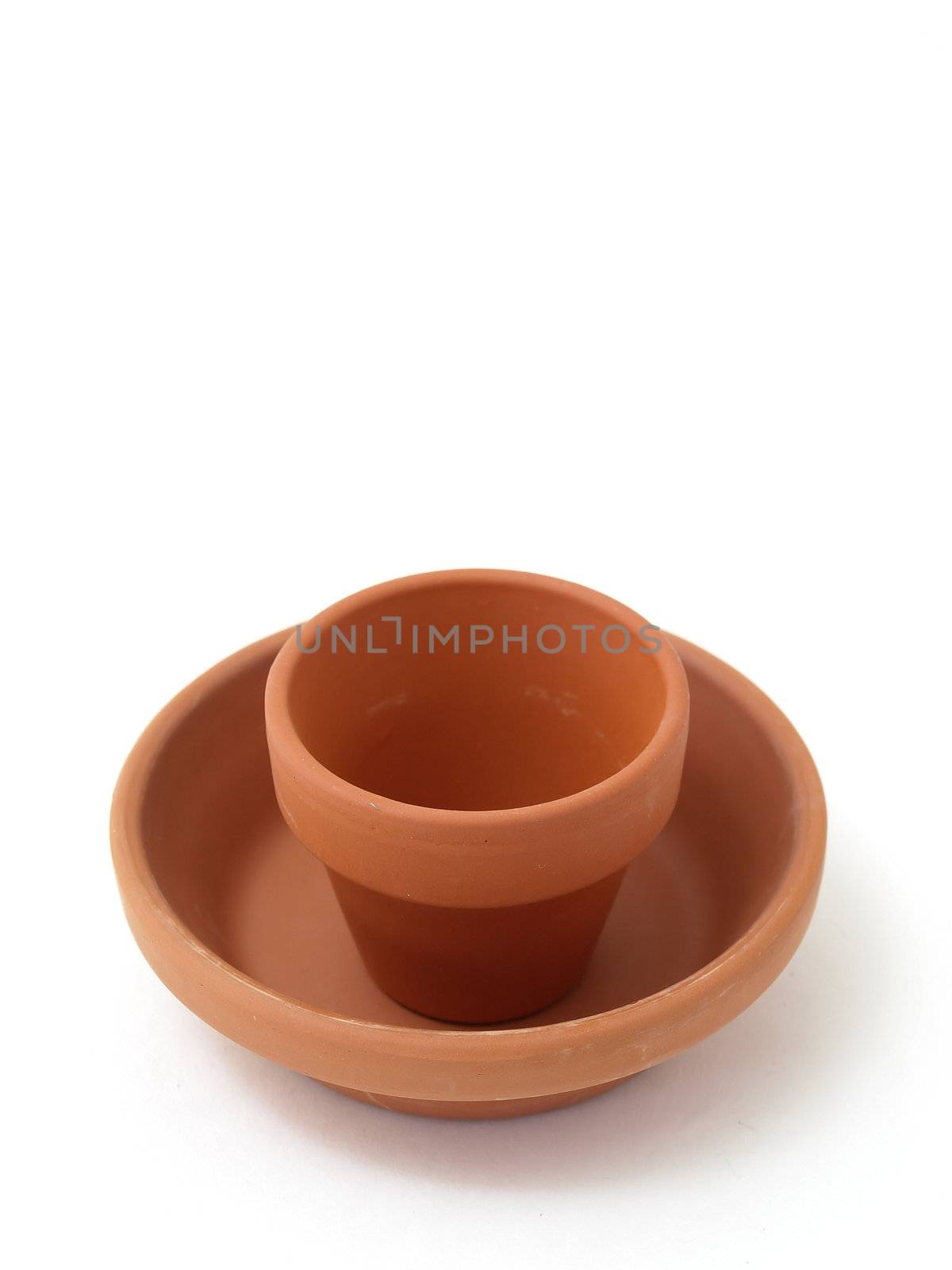 A small terra cotta ceramic pot set in a large saucer. Studio isolated on a white background.