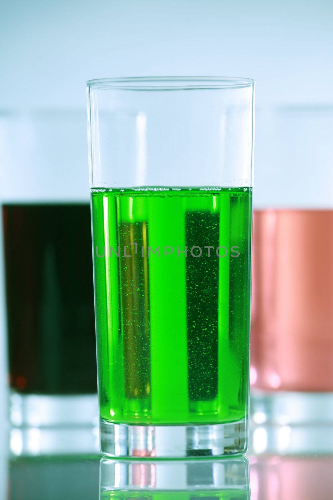 Three glasses with colorful drinks, side by side. blue tones in background