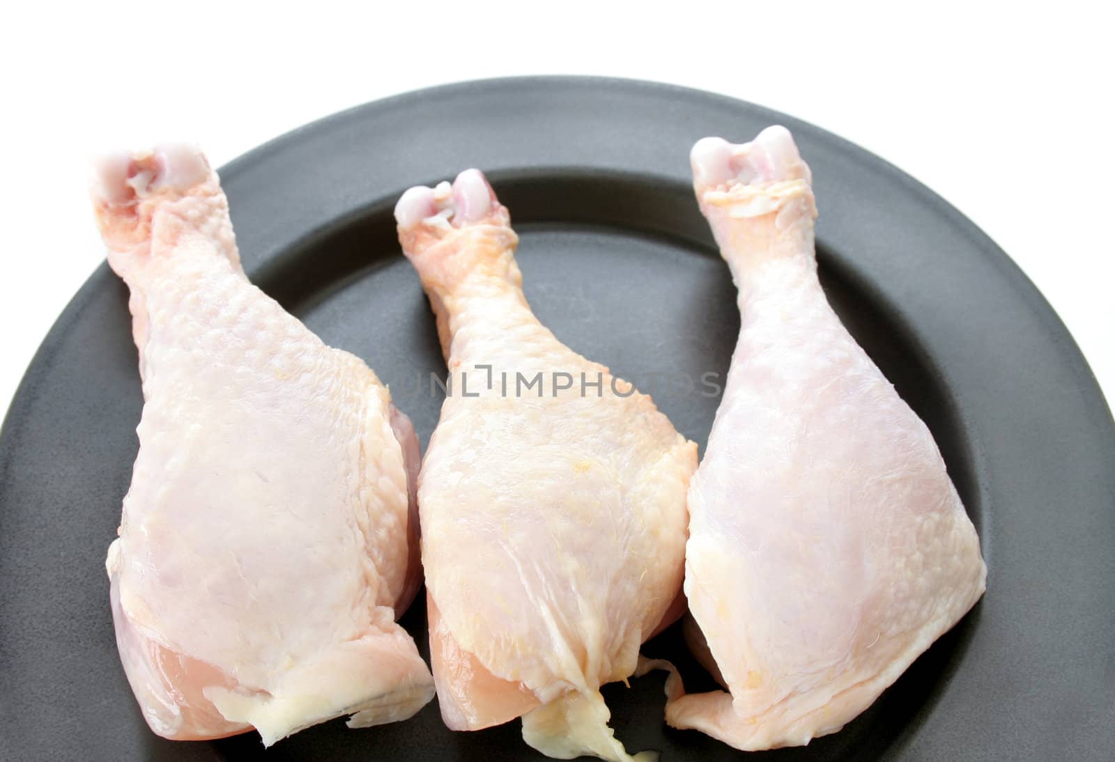 3 raw chicken legs on a plate that is isolated on white.