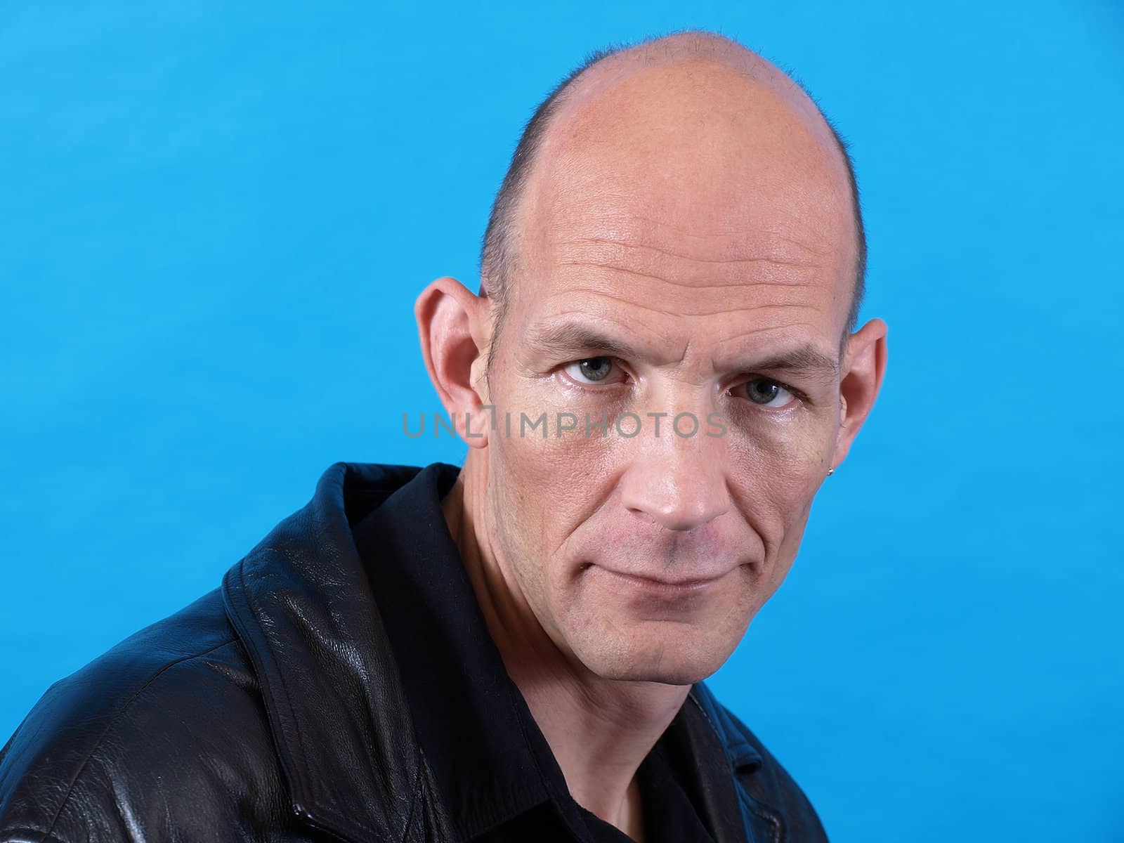 A balding middle aged man isolated against a blue background.