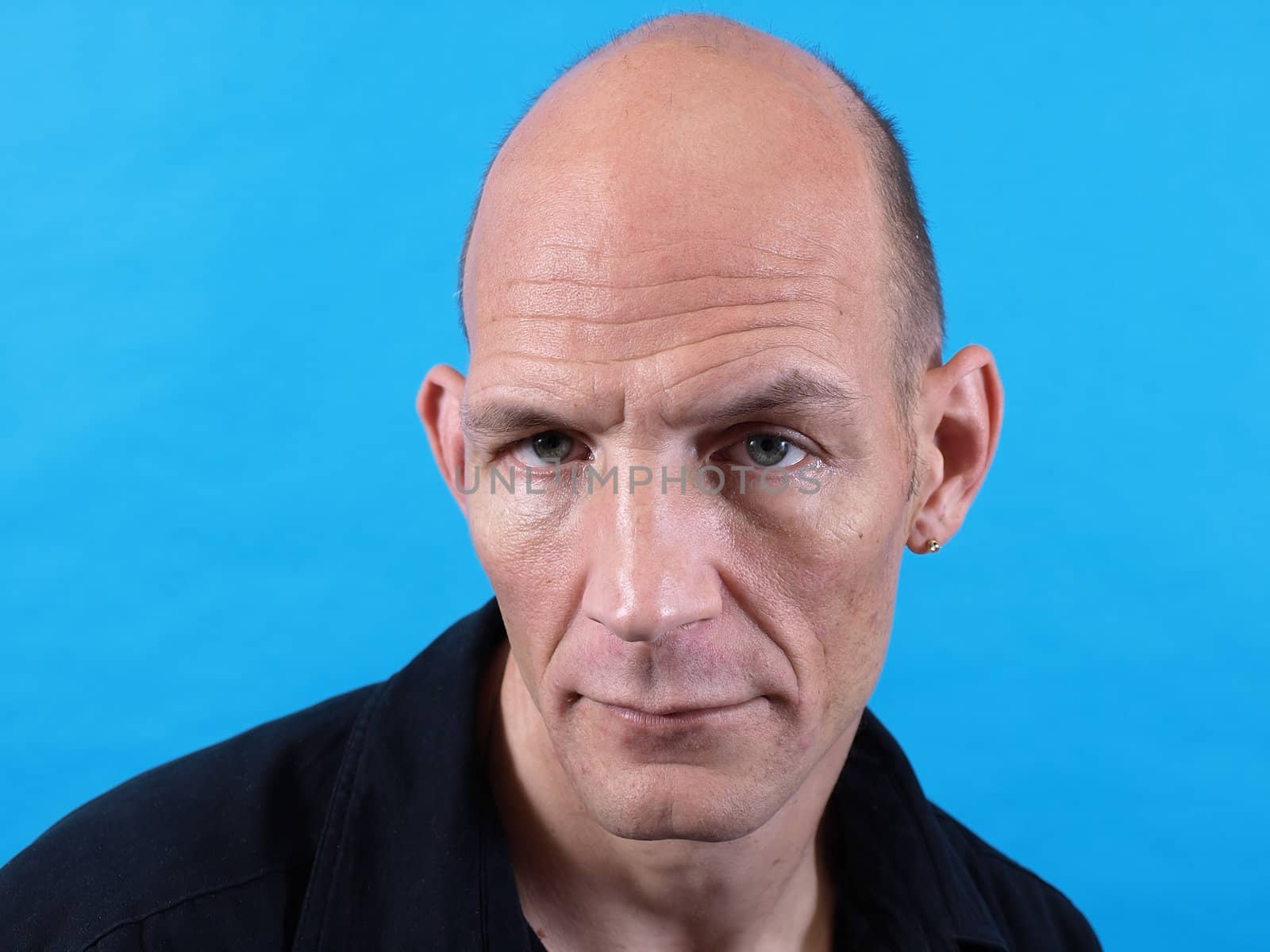 A balding middle aged man isolated against a blue background.