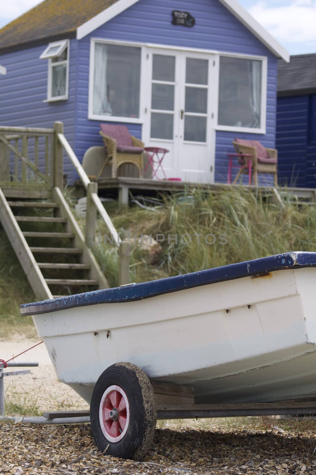 A portrait format image of a blue wooden constructed holiday beach hut with a boat to the foreground. Located at Christchurch, Dorset, England on the South coast.