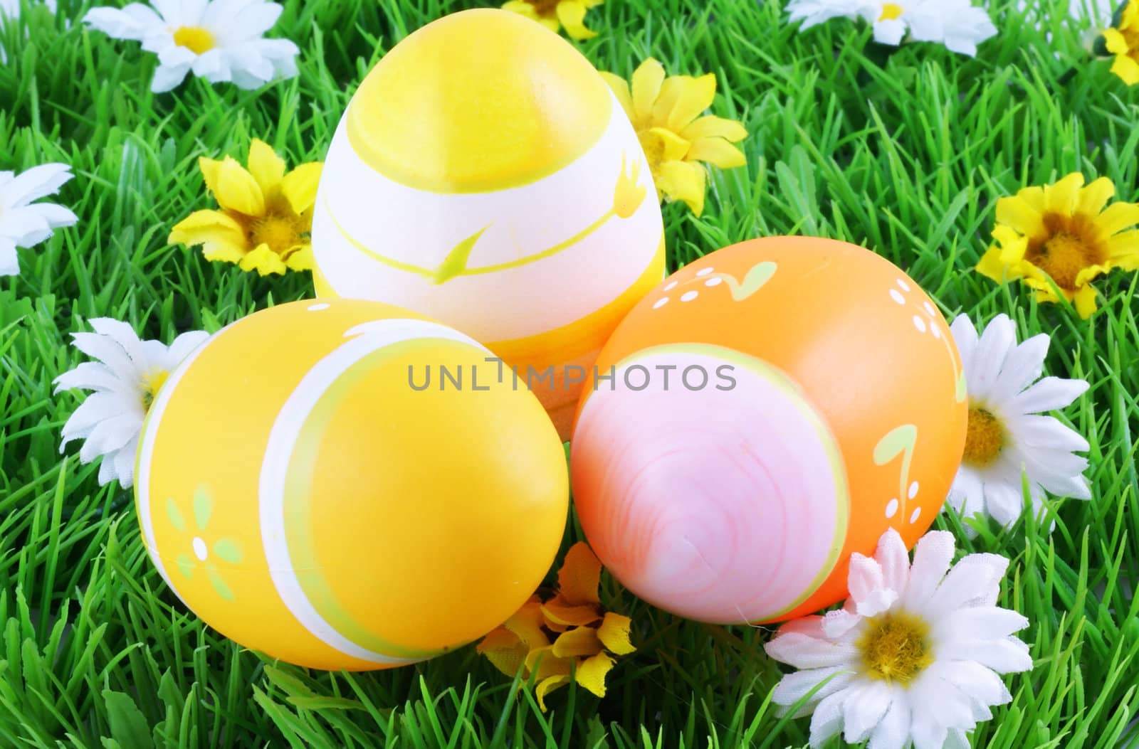 Three easter eggs in grass surrounded by spring flowers.