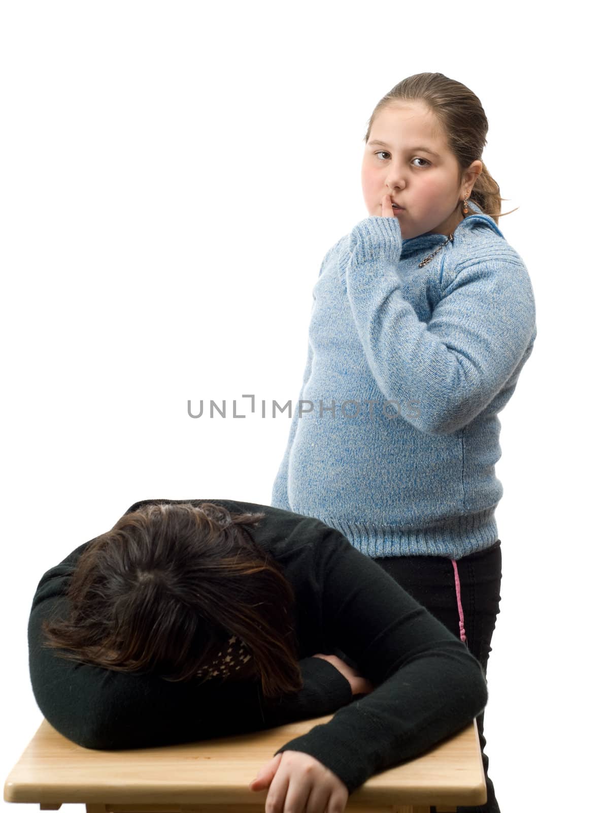 A young girl sneaking up on a friend while she is sleeping at a desk, isolated against a white background