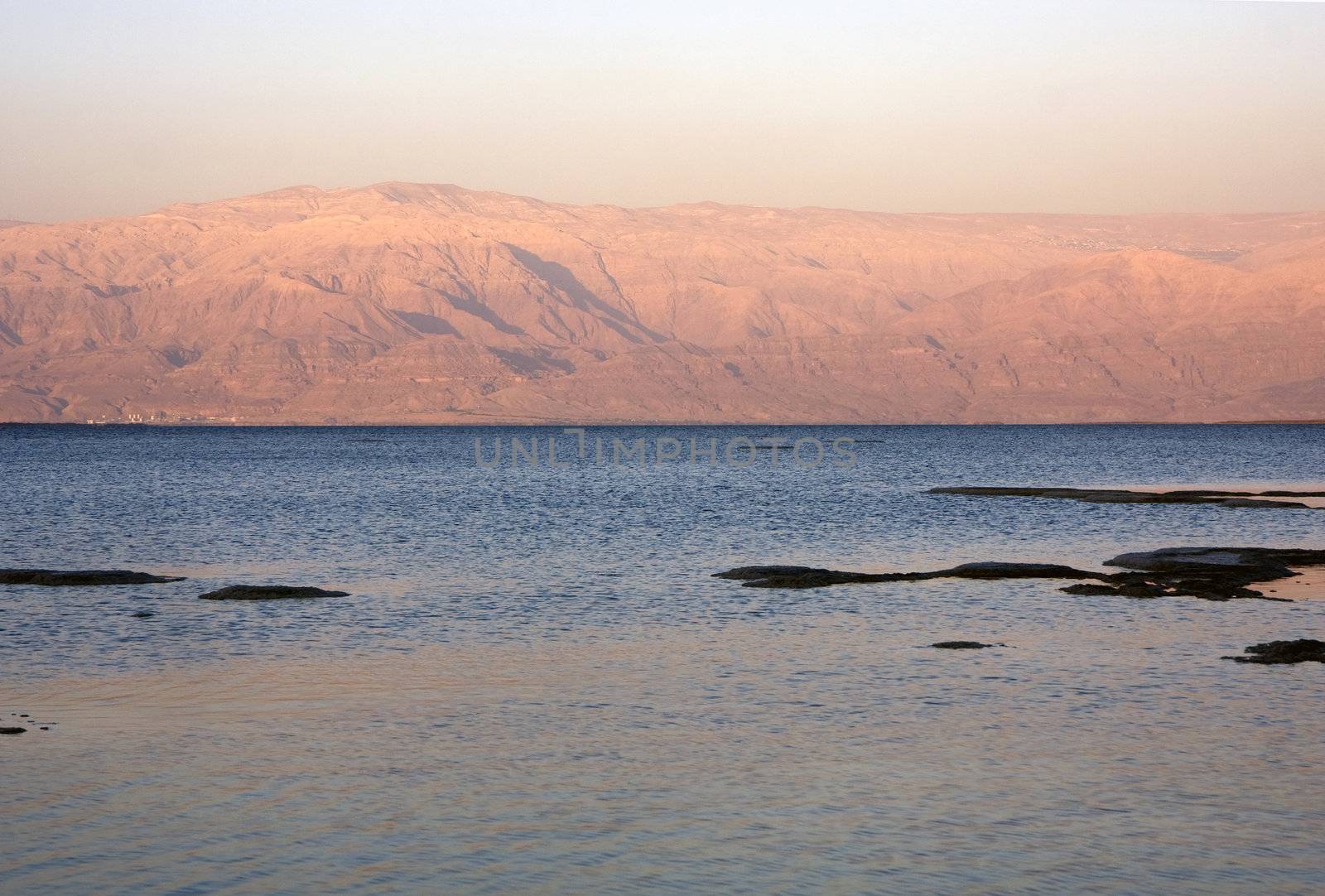 The water of the dead sea with the Jordan mountains and salty islands at sunset