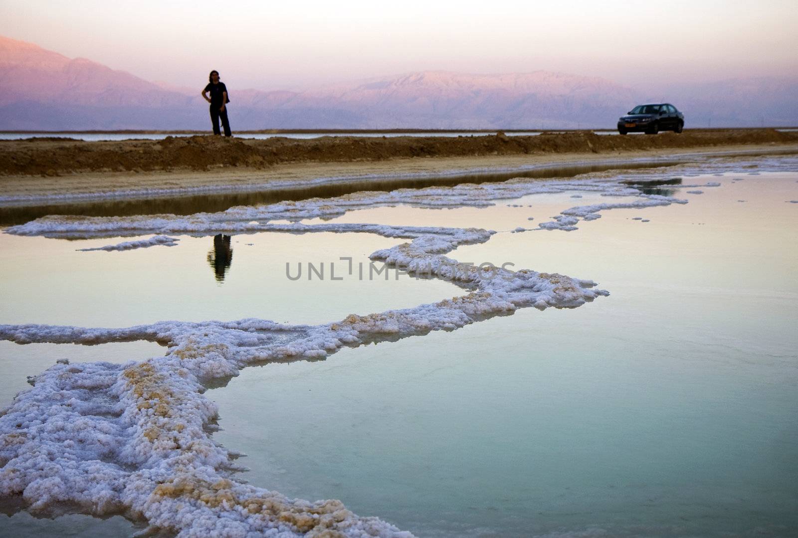 The water of the dead sea with salty paths at sunset and a person and a car