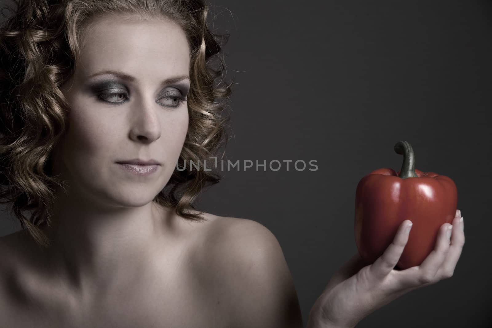 Beautiful young blond woman looking at a pepper in her hand