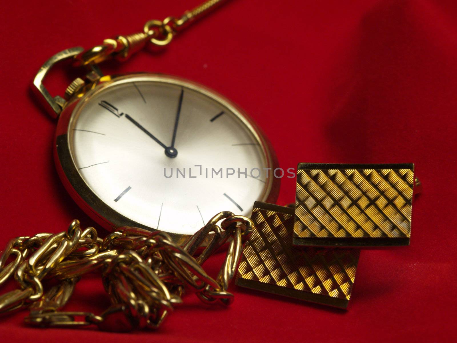 gold pocket watch, necklace and cuff links on red velvet