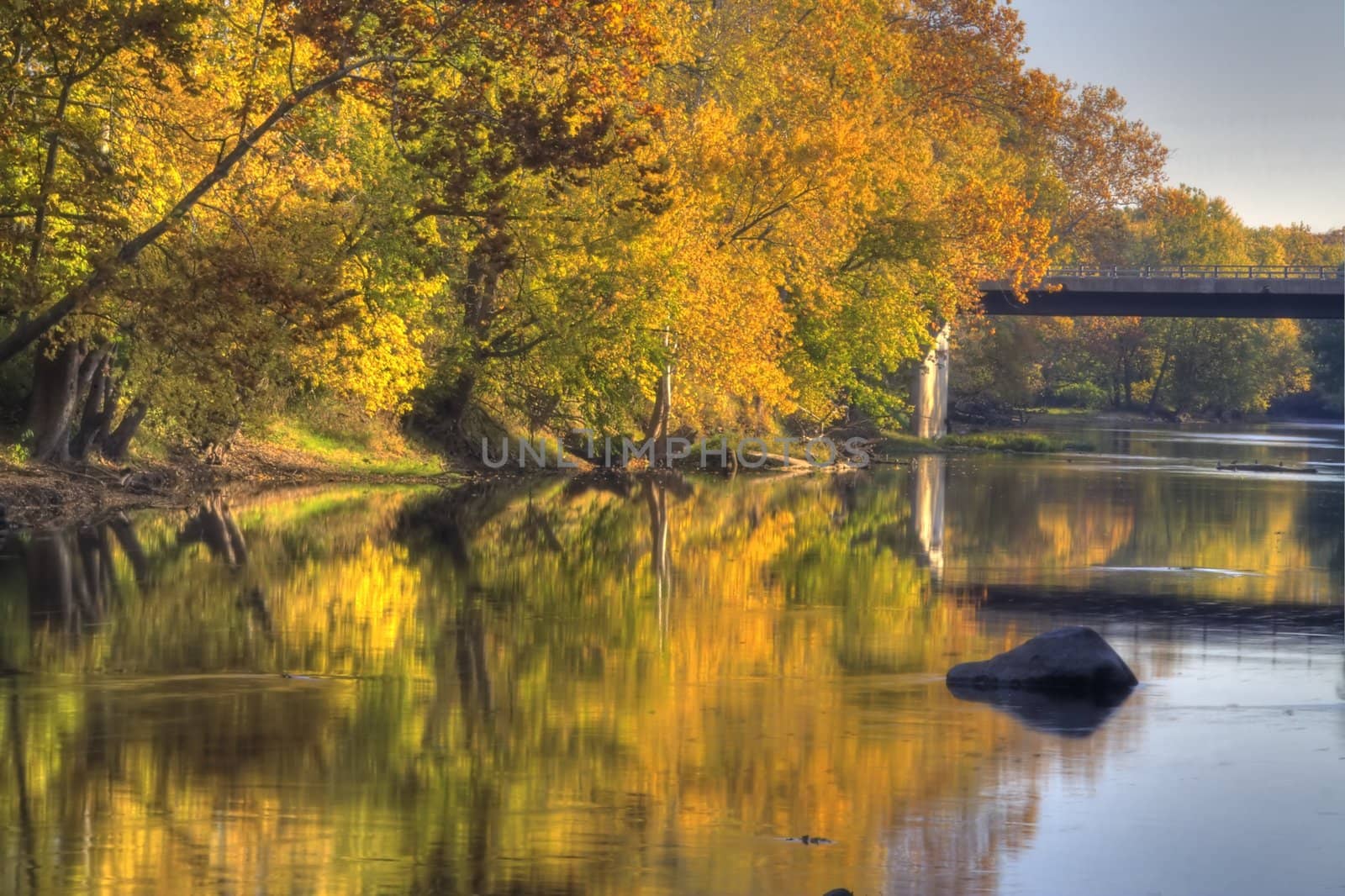 A river flows by brightly colored fall trees with a bridge in the distance.
