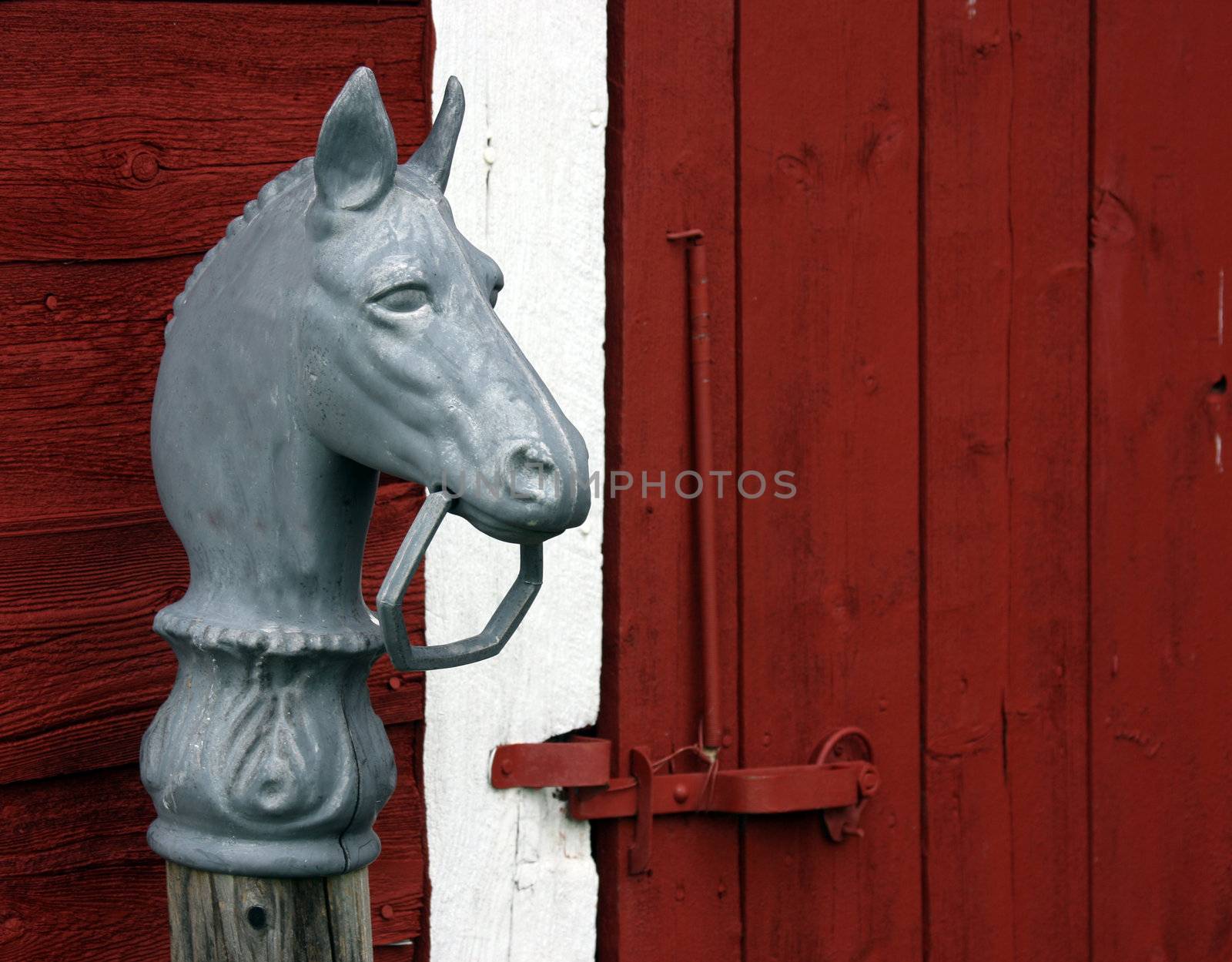 horse hitching post in front of a red barn latched door