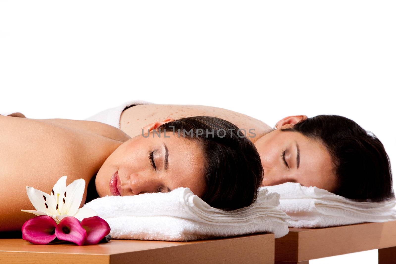Two beautiful women friends laying on wooden tables with head on towels waiting for their massage in the spa, isolated.