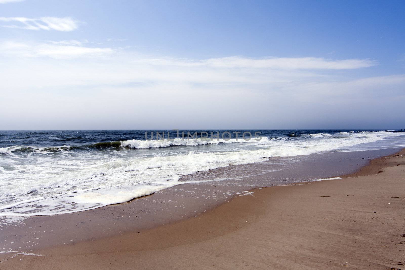 Beautiful beach with ocean sea crashing rolling waves under a blue sky with white clouds, rip currents.