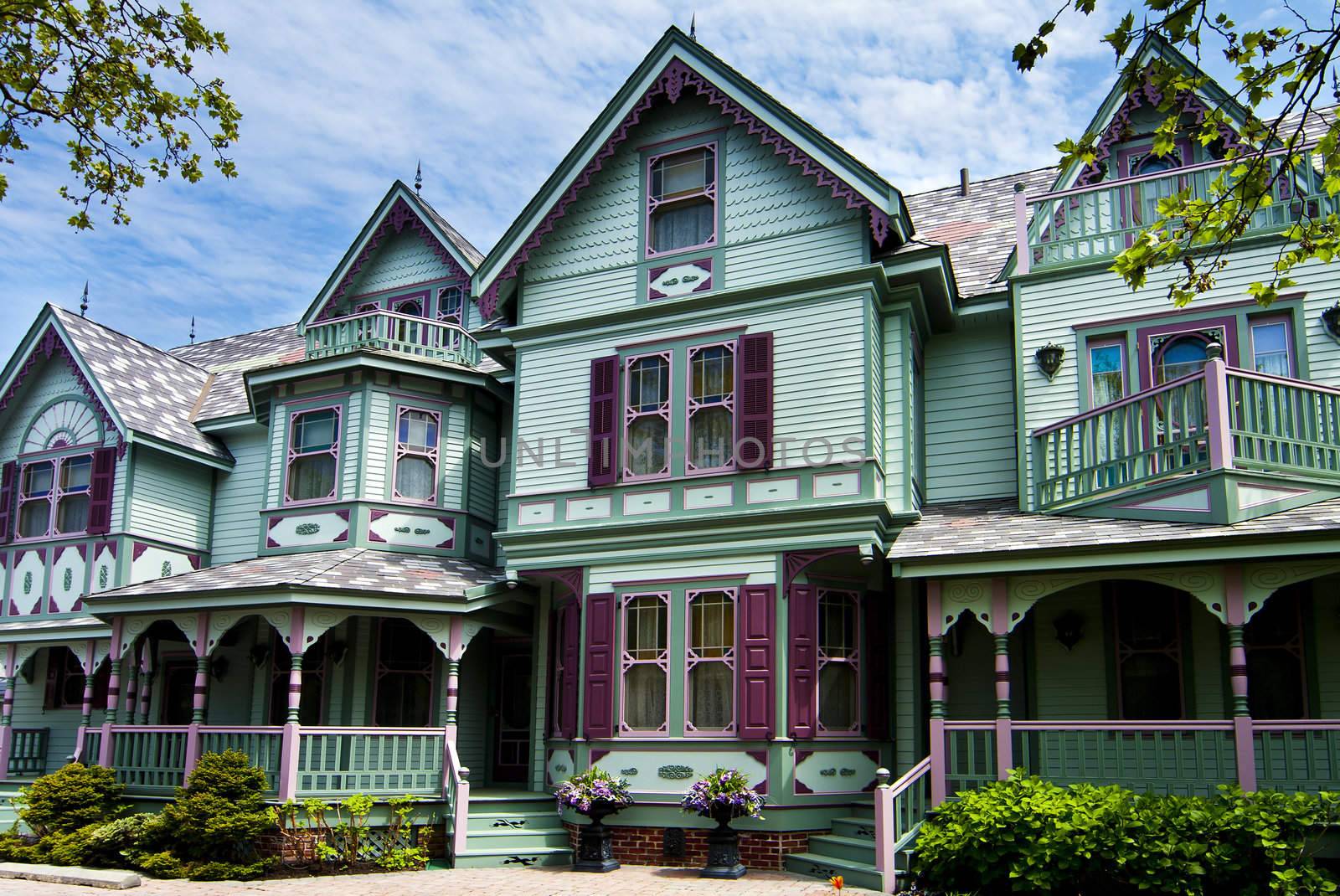 Beautiful big old nostalgic historic wooden green with purple Victorian house building with porch.