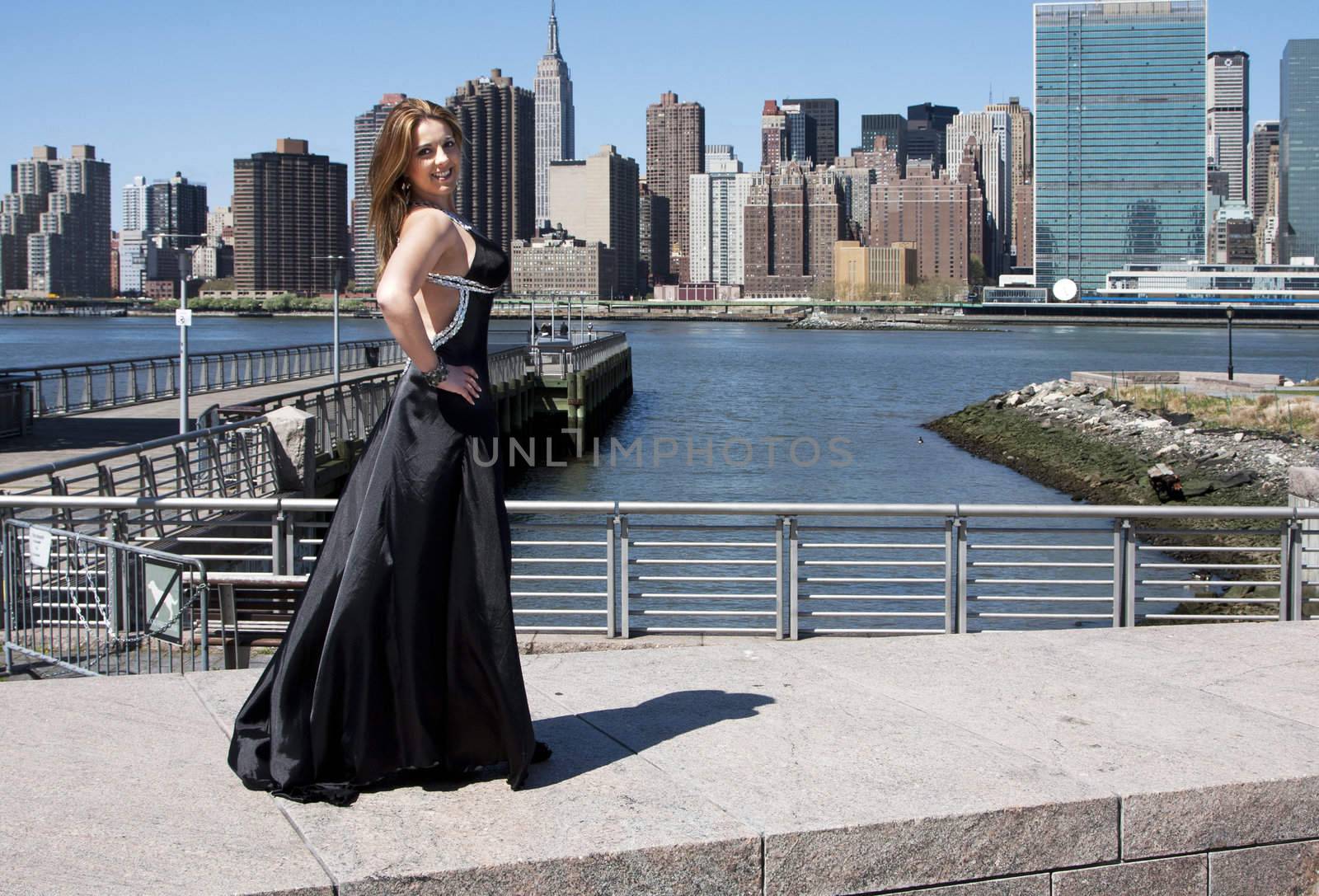 Beautiful happy smiling Caucasian Latina fashion model woman in black evening cocktail dress posing standing in front of skyline of Manhattan, New York City.