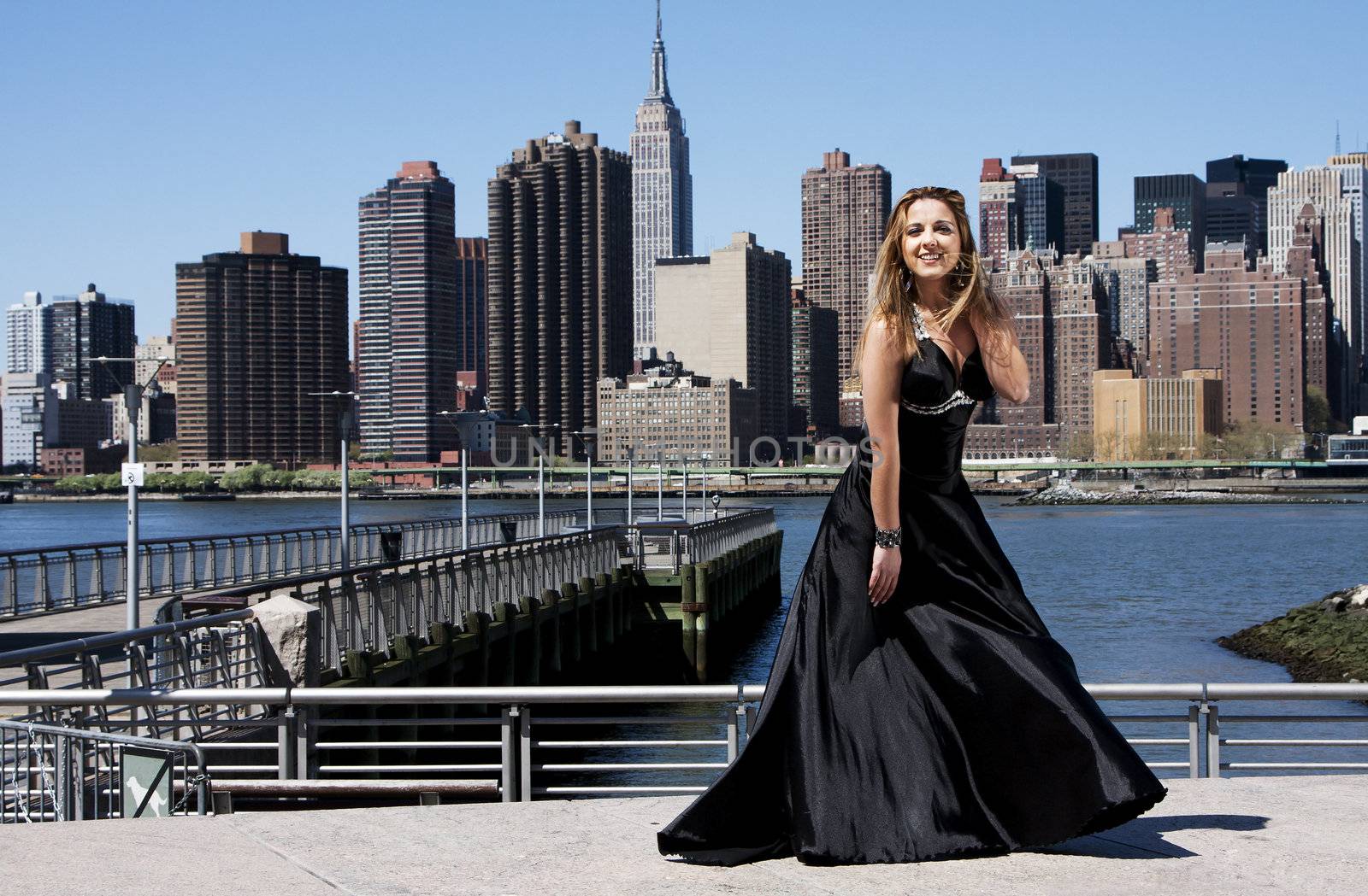 Beautiful happy Caucasian Latina fashion model woman in black evening cocktail dress posing standing in front of skyline of Manhattan, New York City.