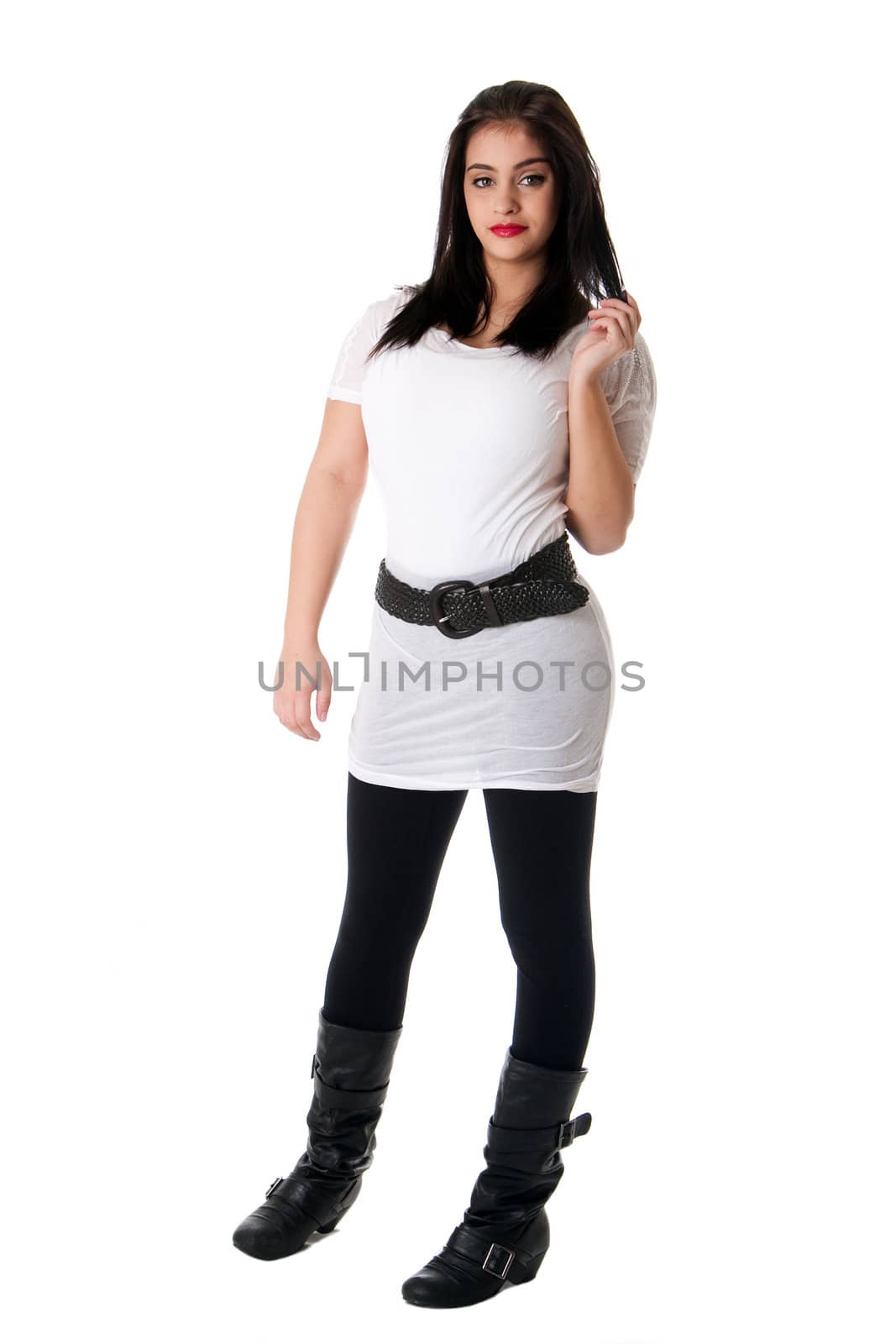 Beautiful playful brunette Caucasian Hispanic Latina woman with red lipstick standing touching her hair, wearing white shirt and black leggings, isolated.