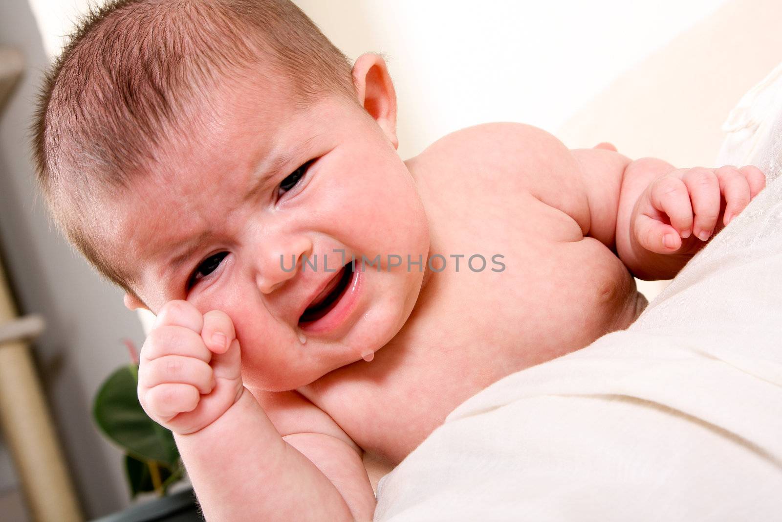 Face of an unhappy unisex Caucasian Hispanic baby crying with tears while rubbing eye.