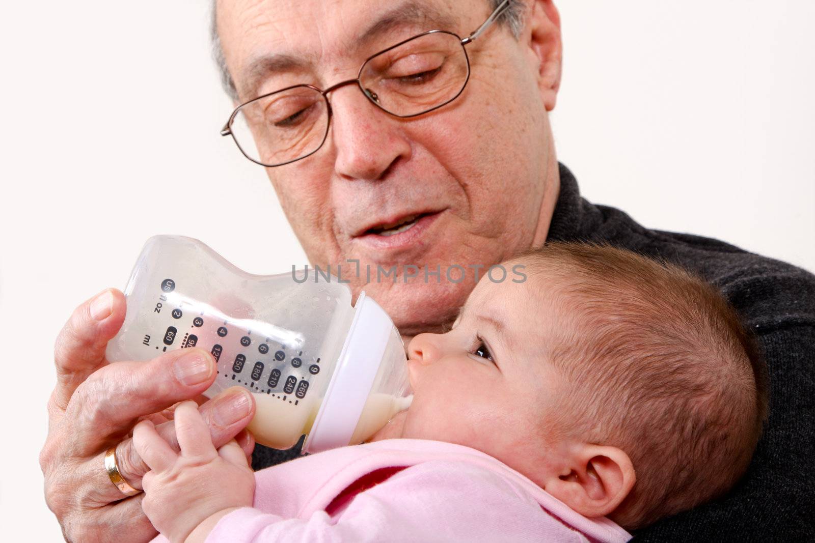 Caucasian Hispanic Grandfather feeding cute baby girl with a bottle of milk while holding infant in his arms.