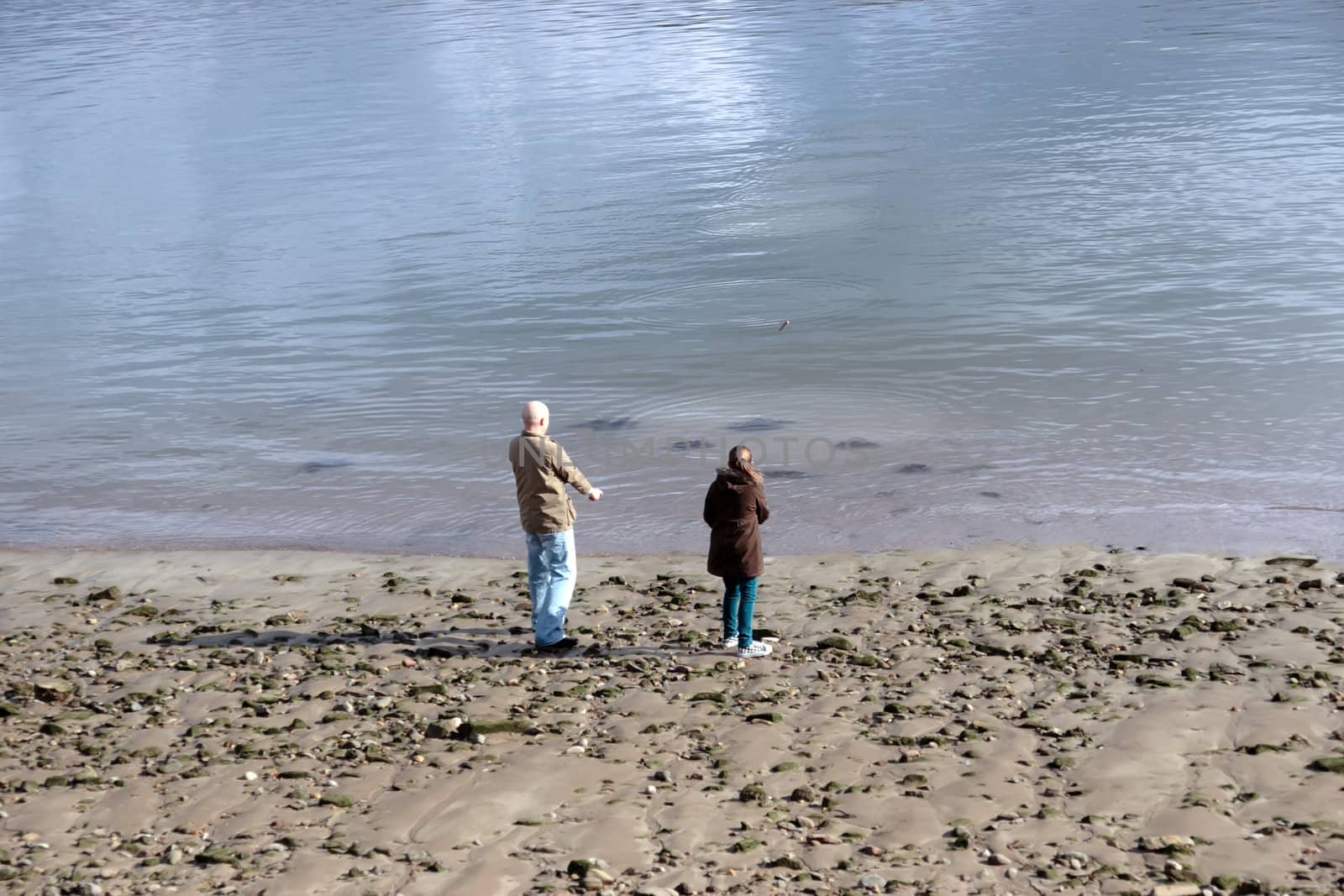 father and daughter skimming stones on the seashore
