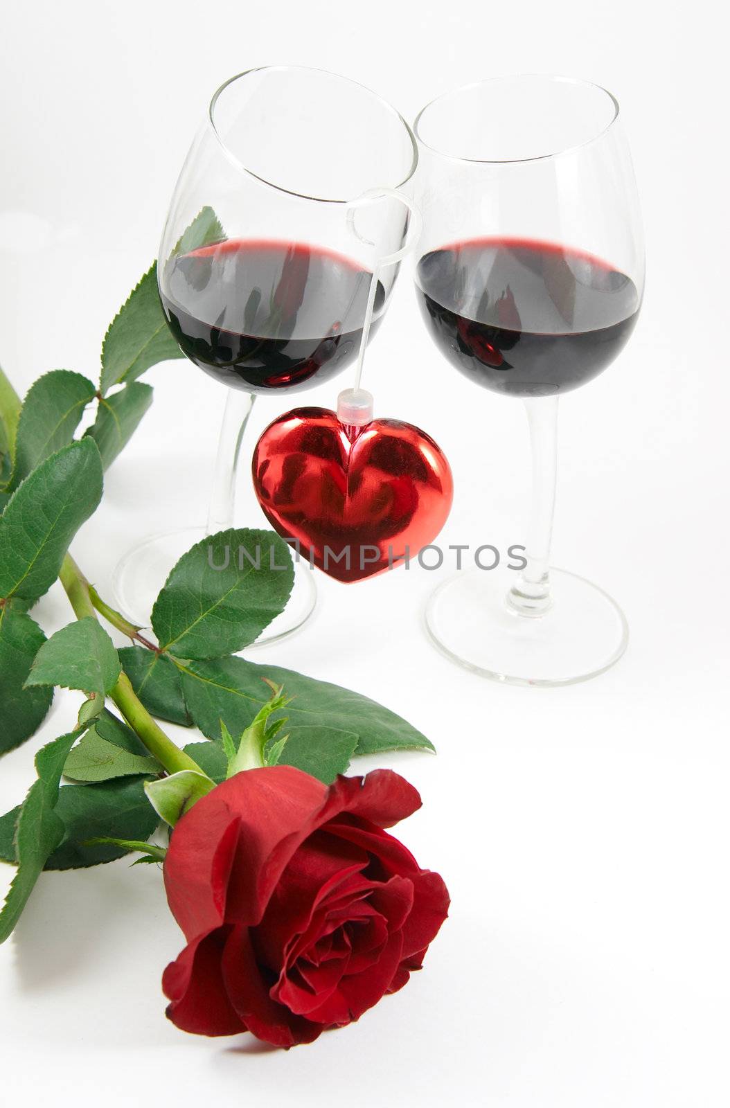 Red rose, heart and two glasses with red wine over white background