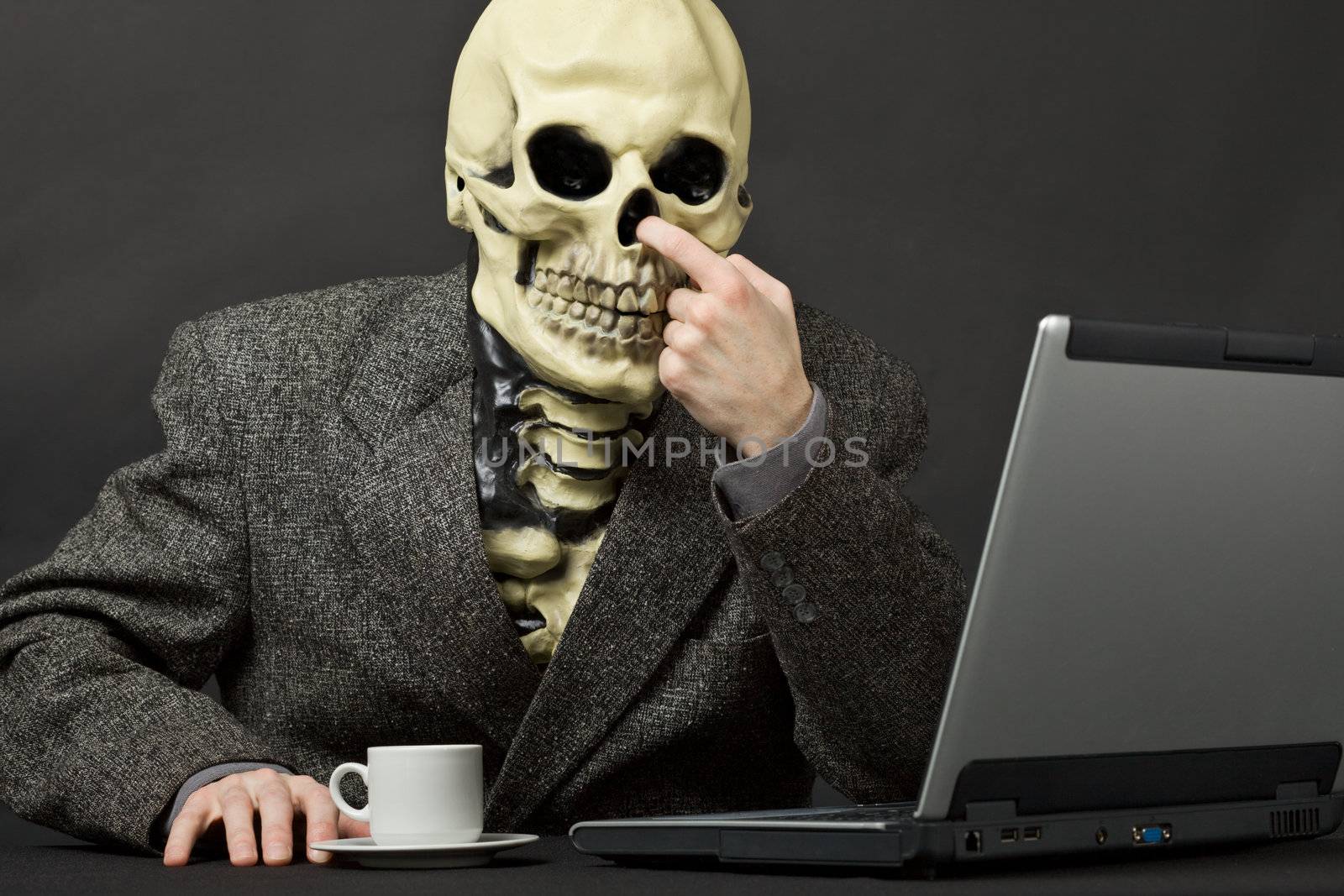 The skeleton picks in a nose on table with laptop