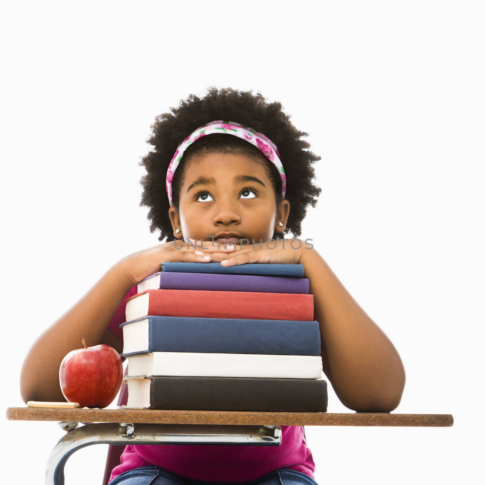 African American girl sitting in school desk with large stack of books looking bored.