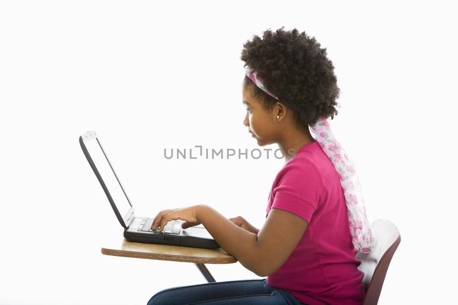 Side view of African American girl sitting in school desk typing on laptop computer.