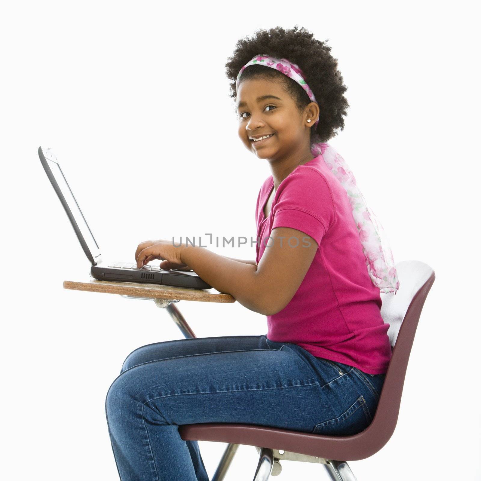 African American girl sitting in school desk typing on laptop computer smiling at viewer.