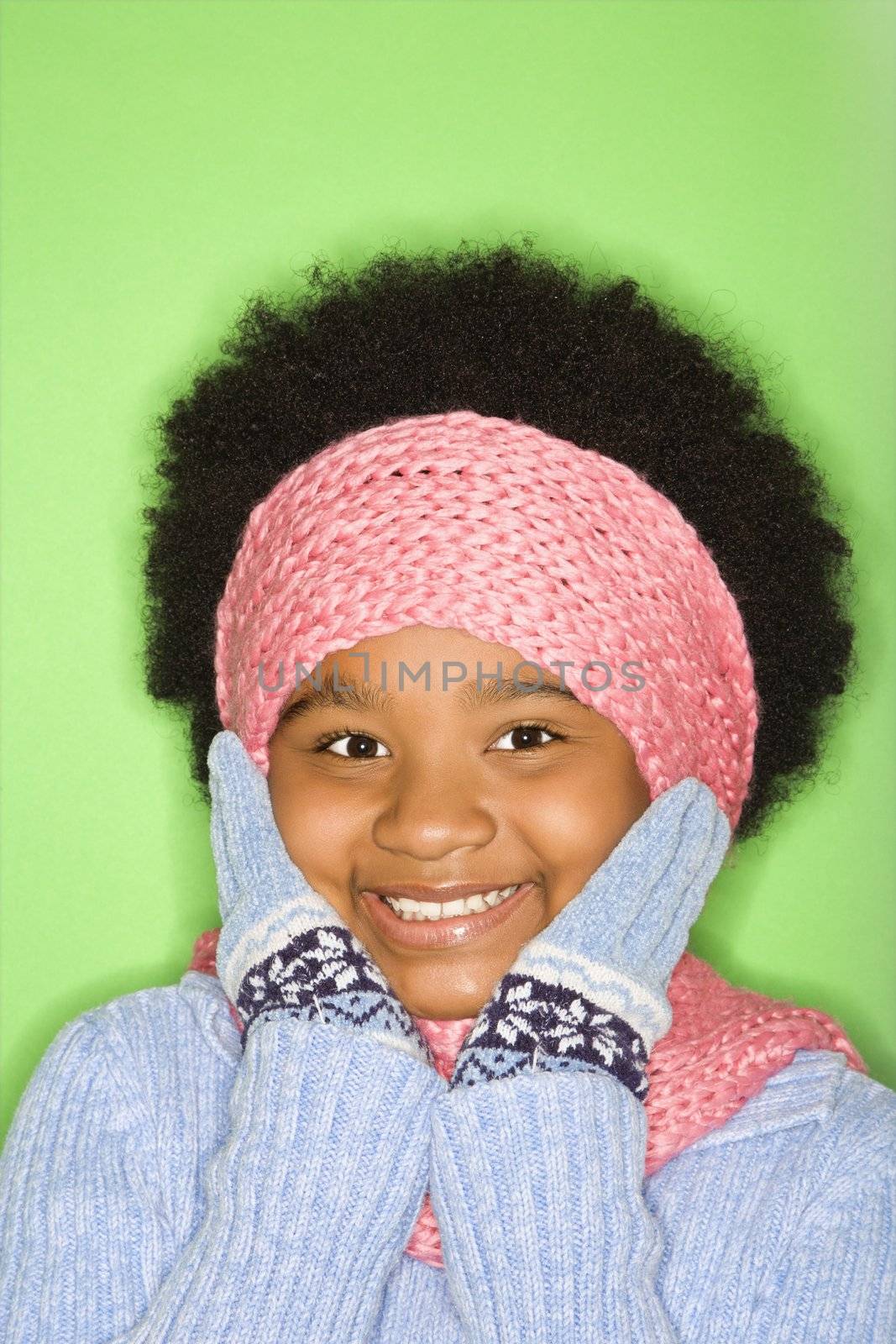 African American girl in winter clothing with gloved hands to face smiling at viewer.