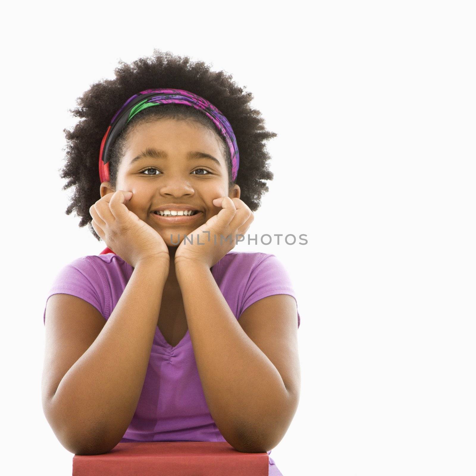 African American girl with head resting on hands smiling at viewer.