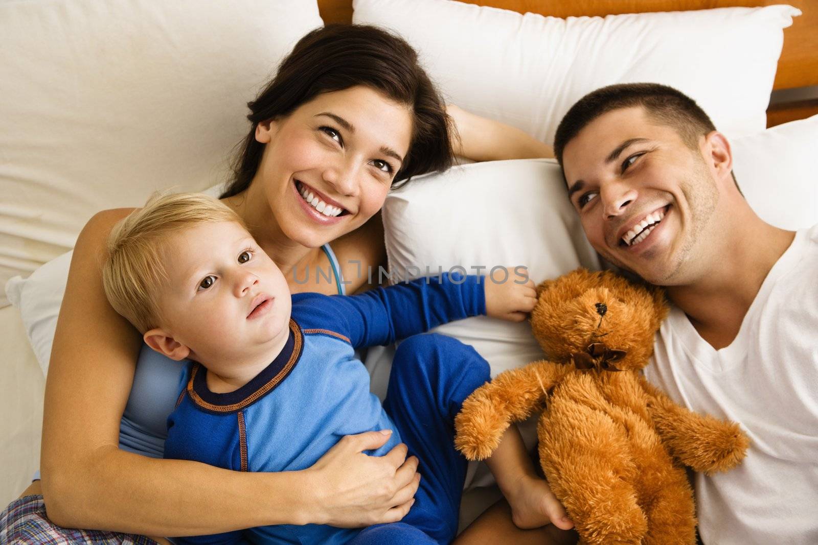 Caucasian parents and toddler son lying in bed smiling.