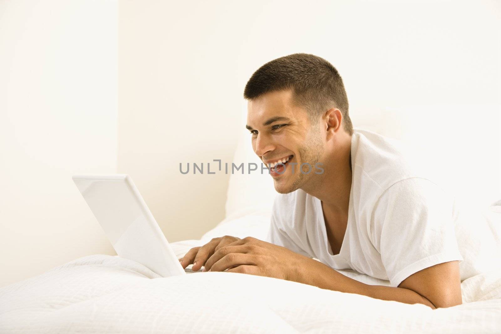 Handsome Caucasian mid adult man lying in bed with laptop.