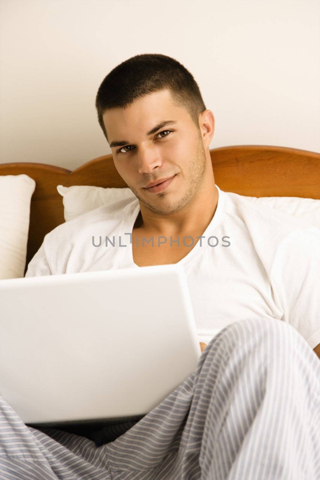 Handsome Caucasian mid adult man sitting in bed with laptop looking at viewer.