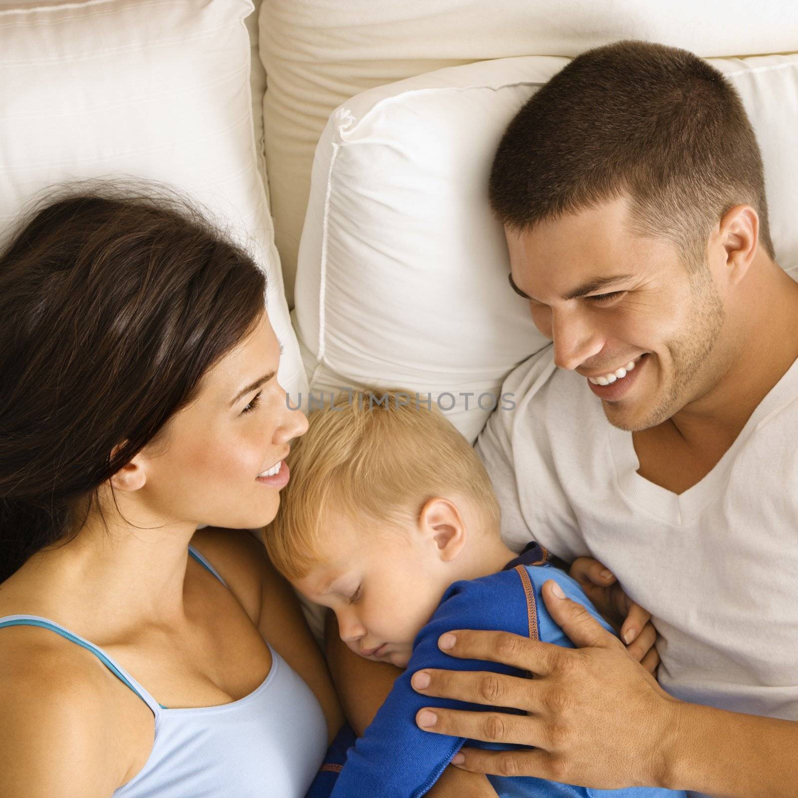Caucasian mid adult parents with toddler son sleeping in bed.