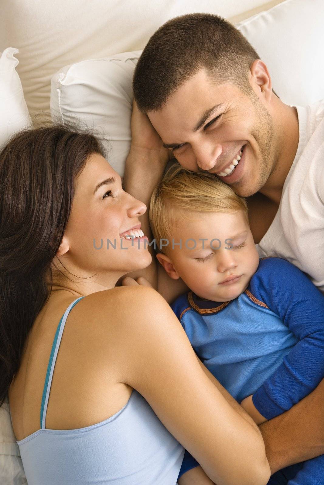 Caucasian mid adult parents cuddling with toddler son sleeping in bed.