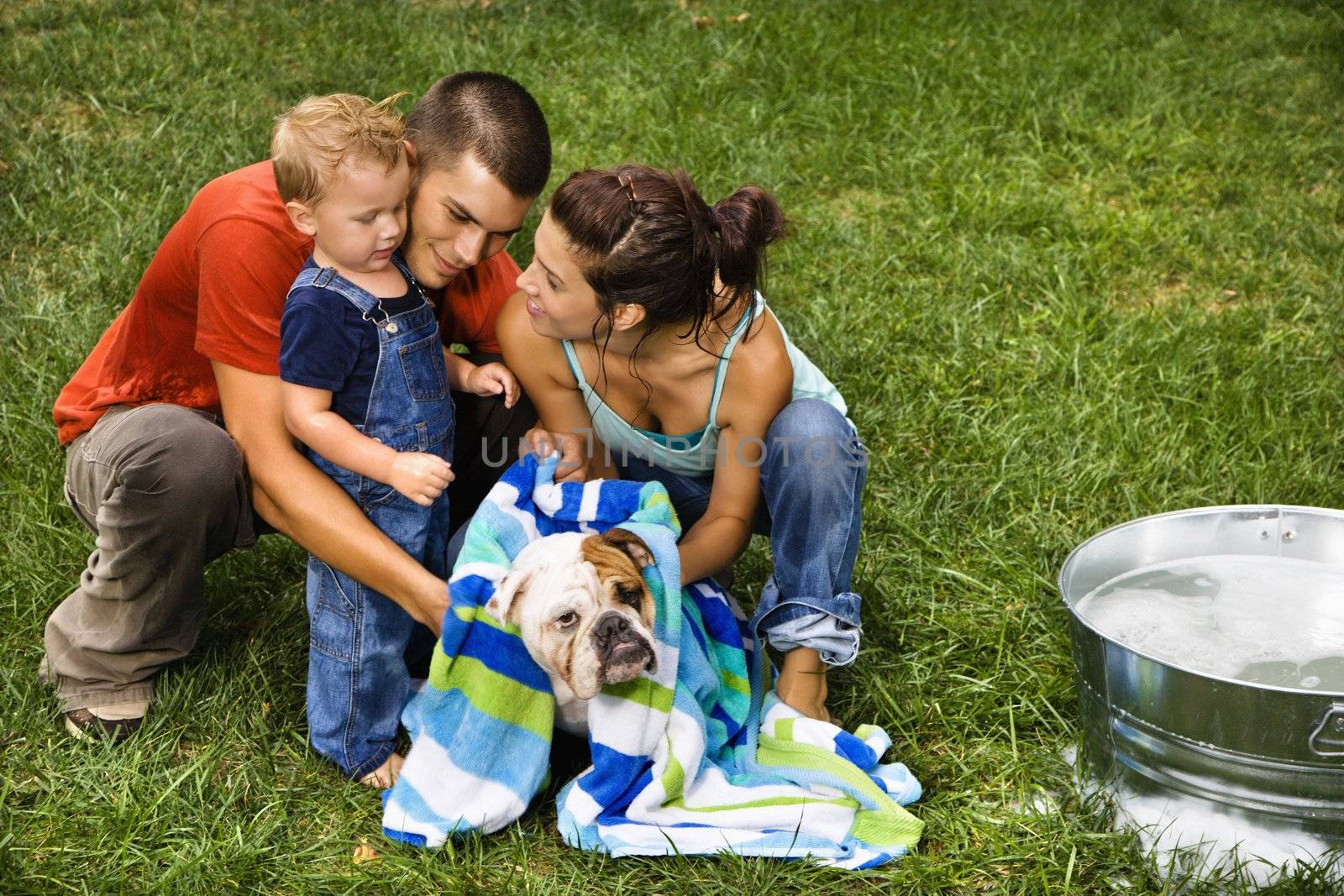 Caucasian family with toddler son drying English Bulldog with towel after a bath outdoors.