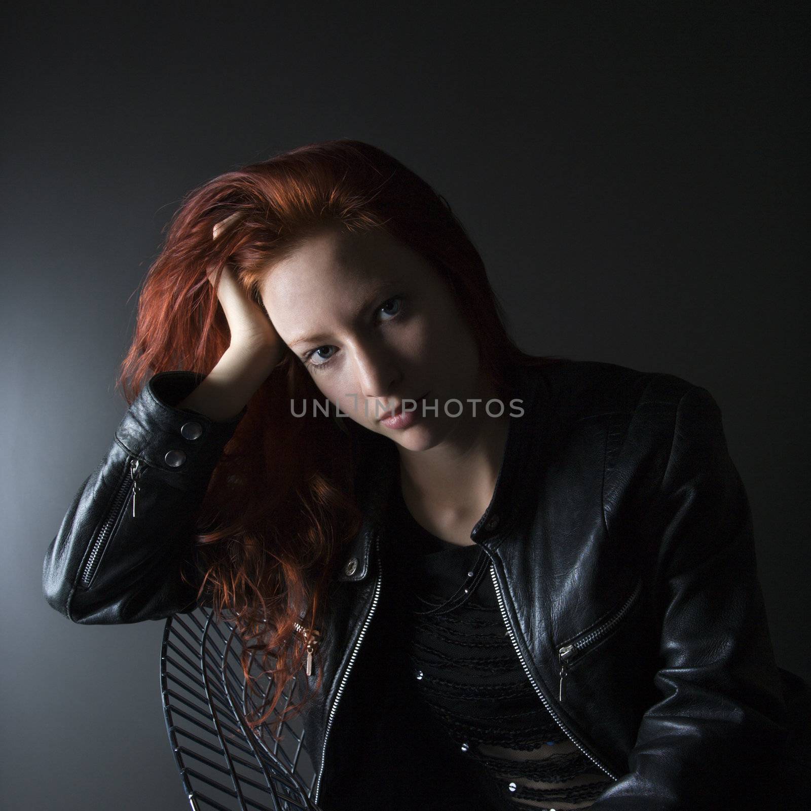 Portrait of pretty redhead young woman sitting in chair resting head on hand.