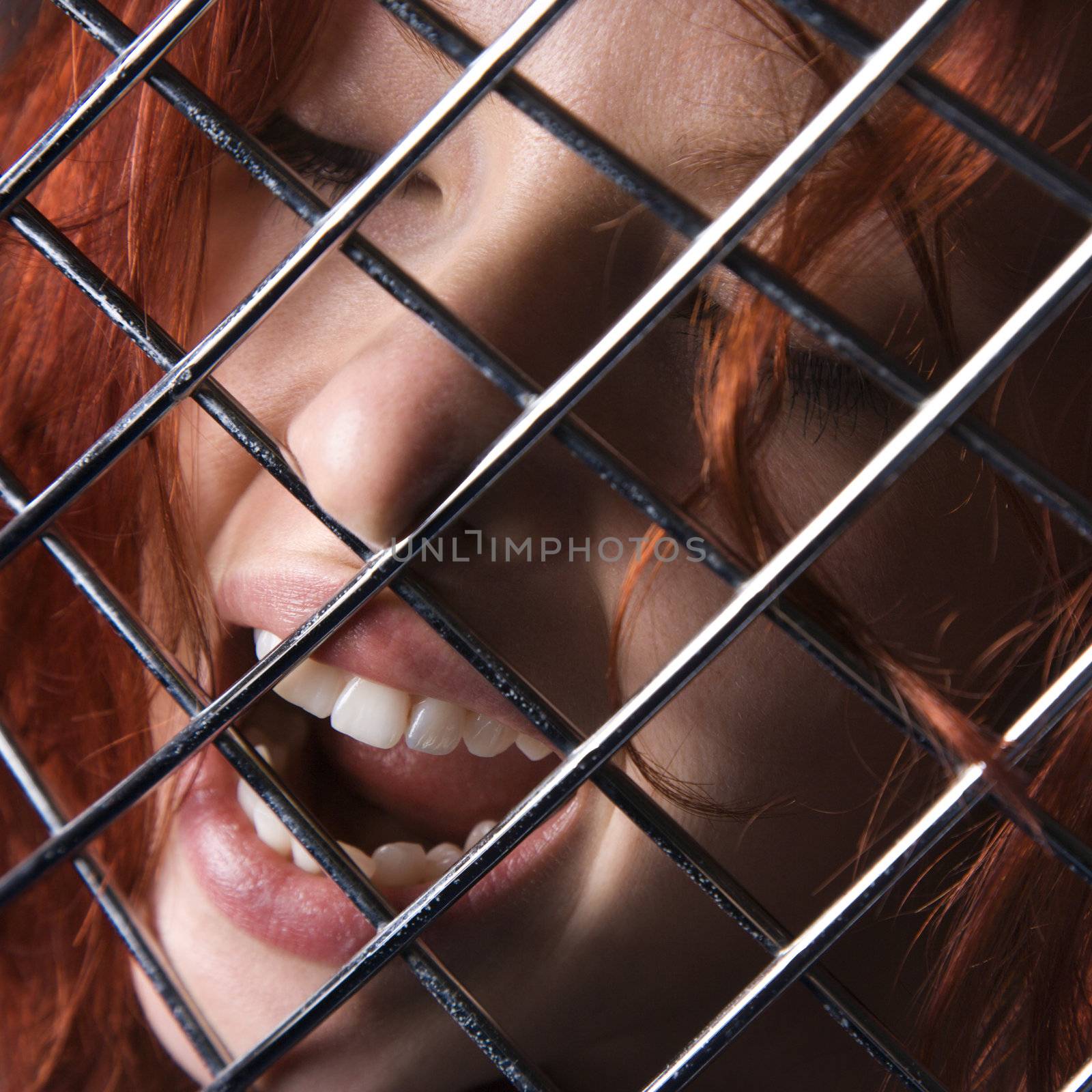 Pretty redhead young woman face with mouth open behind metal pattern.