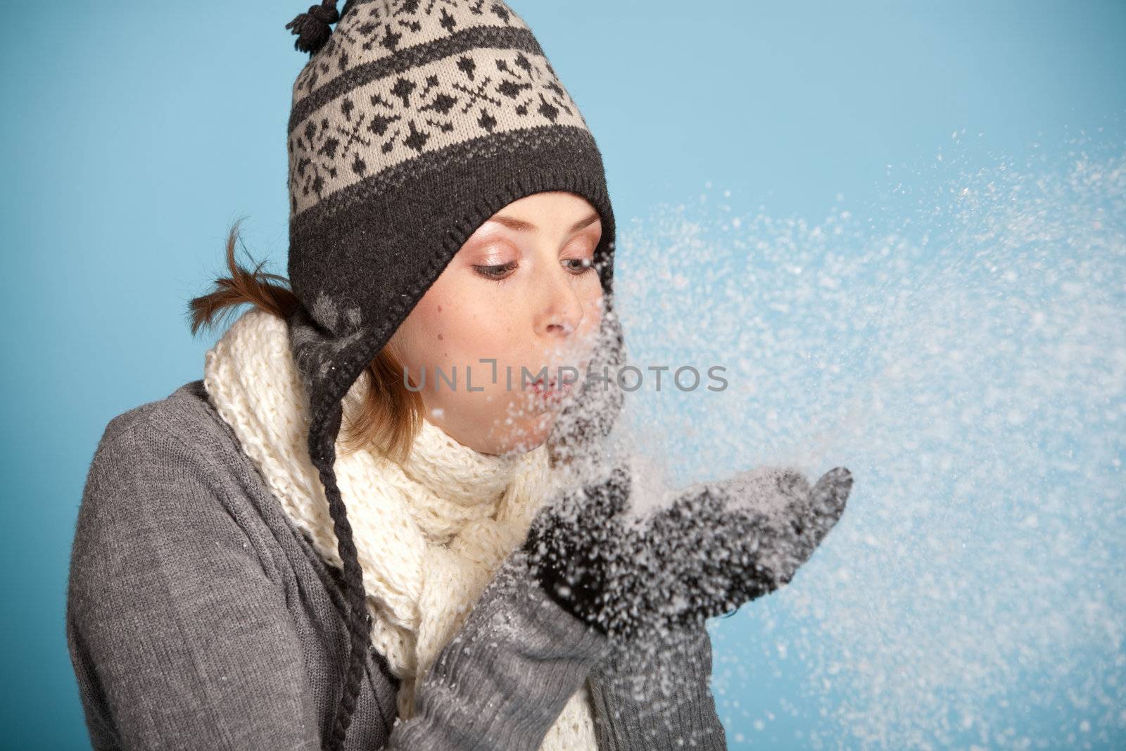 Pretty blond girl with winter clothes blowing snow from her hands