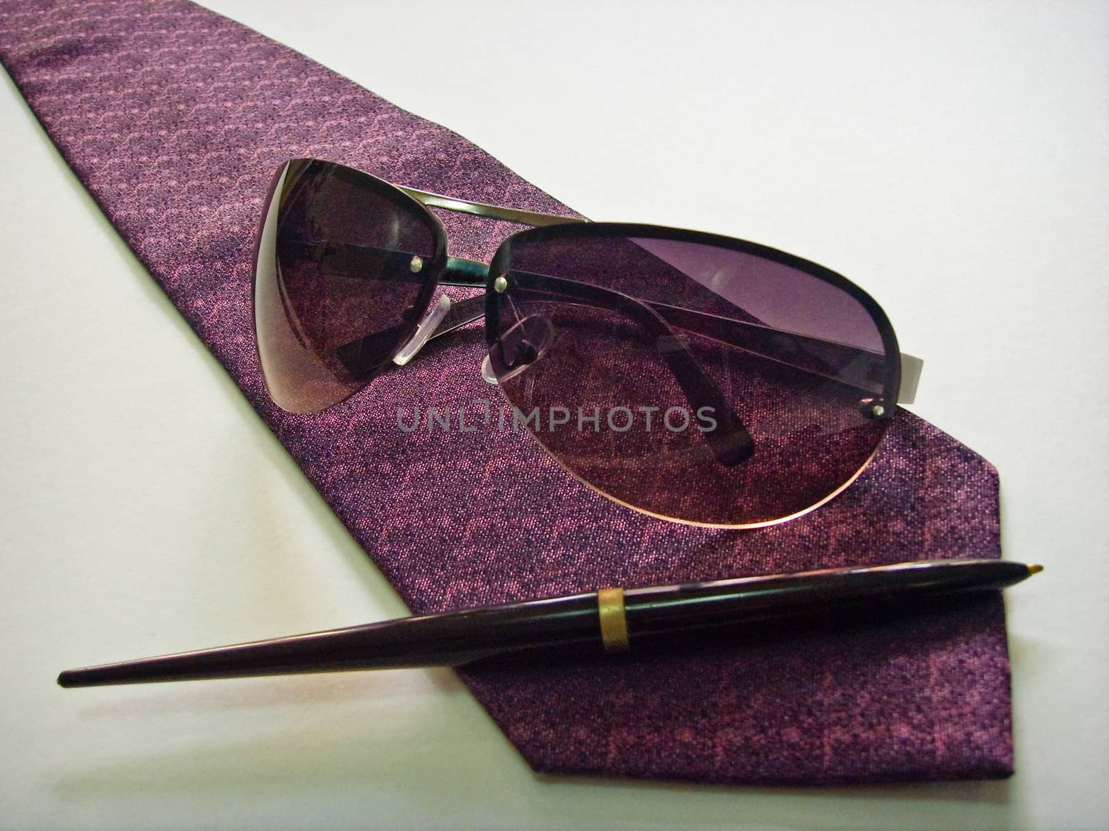 Sunglasses, pen and a purple tie on a white background