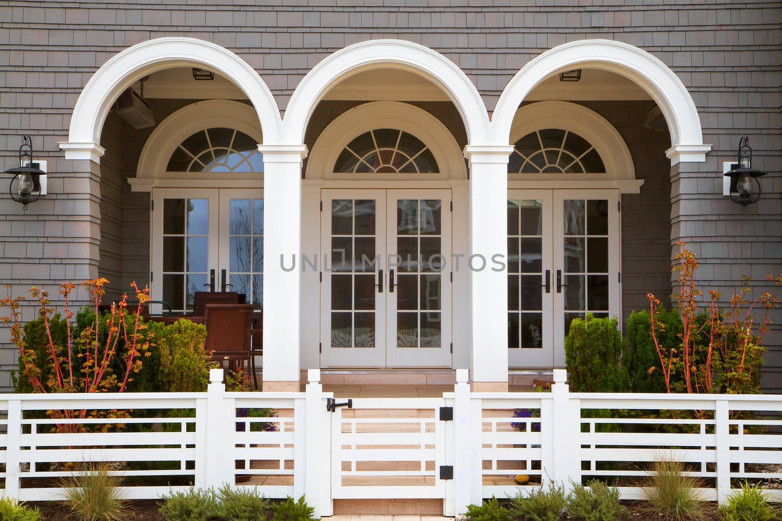 Three french door entrance to grey house with white trim and deco style fence